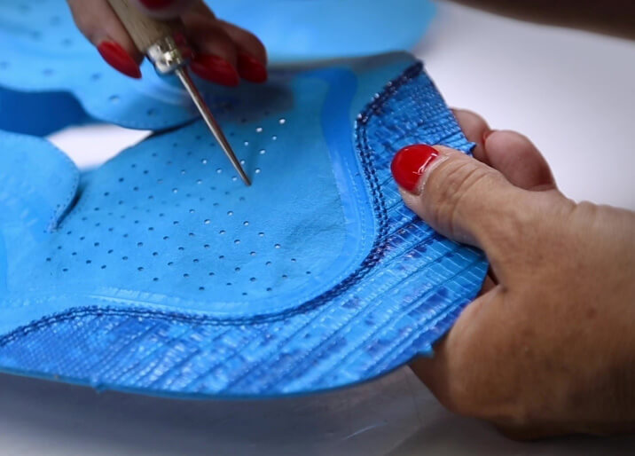 Italian woman making perforations in nubuck leather upper of Courser luxury sneakers